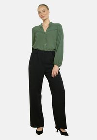 Blusa verde con bottoni, pannello testurizzato, maniche lunghe e colletto, abbinata a pantaloni neri a gamba larga e tacchi neri.