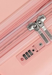 Valigia rosa chiaro con superficie testurizzata, doppi zip argento e serratura combinata integrata per la sicurezza.