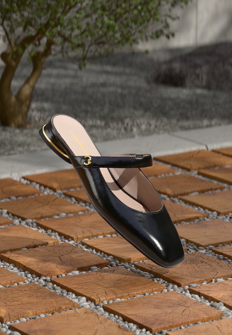 Sort laklæderslingback-sko med firkantet tå, en tynd ankelrem og en gulddetalje på hælen, vist over træfliser.