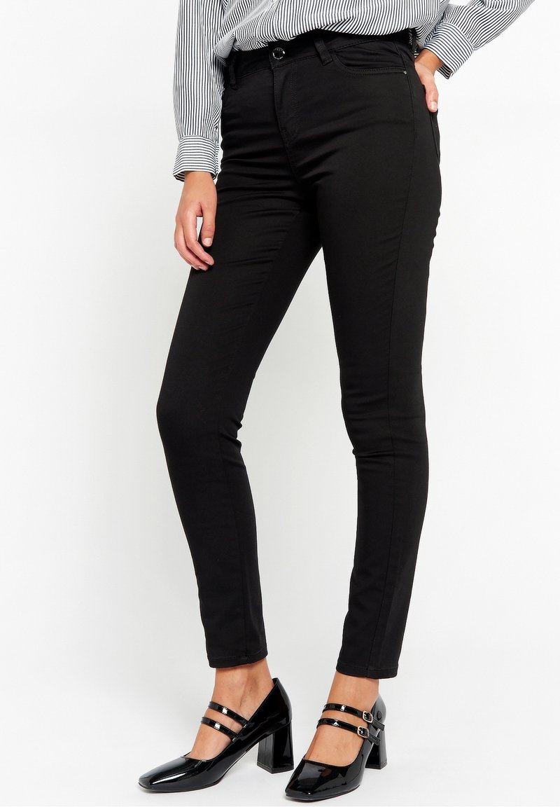 Pantalon noir slim porté avec des chaussures à talons blocs en cuir verni noir à doubles brides et une chemise rayée manches longues.