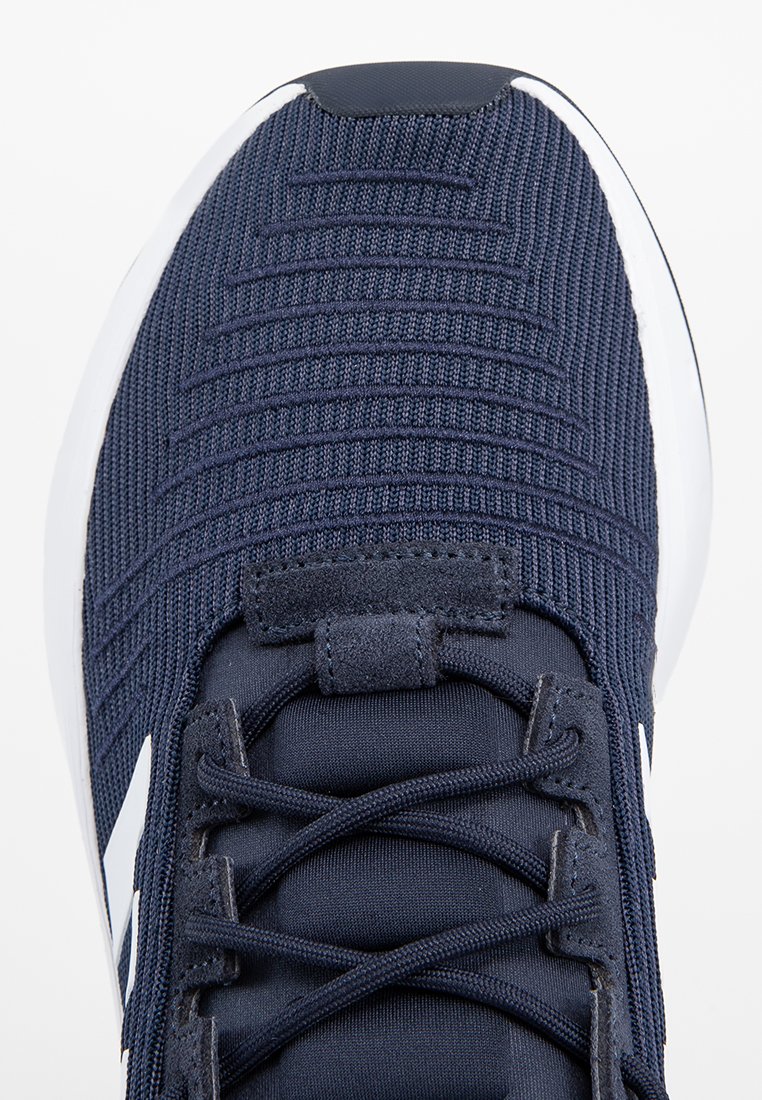 Marineblaue Sportschuhe mit strukturiertem Strick-Obermaterial, schwarzen Schnürsenkeln und weißer Sohle, von oben fotografiert, wobei der Zehen- und Schnürbereich sichtbar ist.