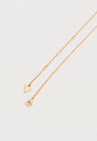 Κολιέ σε χρυσό τόνο με λεπτή αλυσίδα, που διαθέτει τρίγωνο μενταγιόν με τη λέξη "GUESS" και κούμπωμα με κλιπ αστακού.