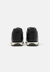 Black leather sneakers featuring white midsole, textured soles, and rear pull tabs. Classic athletic design with lace-up front.