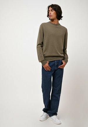 Oliwkowy sweter dzianinowy z długimi rękawami, zestawiony z ciemnoniebieskimi dżinsami i białymi sneakersami. Prosty, casualowy design o luźnym kroju.