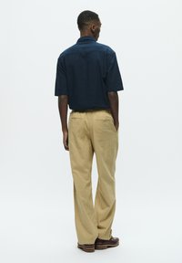 C�ămașă marină cu mânecă scurtă și pantaloni largi bej. Cămașa are un guler structurat, iar pantalonii au buzunare laterale și o croială confortabilă. Pantofi maronii.