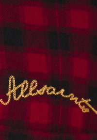 Tessuto a quadri rosso e nero con un aspetto testurizzato, che presenta un logo "Allsaints" ricamato in oro in basso a destra.