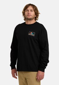 Maglietta nera a maniche lunghe con collo rotondo, featuring una toppa logo multicolore sul petto. Realizzata in tessuto morbido, con una vestibilità rilassata.