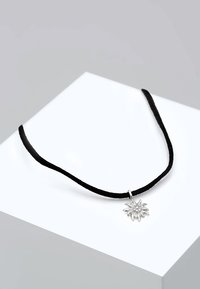 Svart mockahalsband med en silverfärgad solformad hängande detalj som har texturerade strålar och små runda accenter. Enkel och minimalistisk design.
