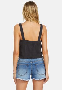 Mustapintainen neulecrop-toppi, jossa on paksut hihnat, teksturoitu pinta ja lyhyt helma, yhdistettynä sinisiin denimshortseihin, joissa on repaleiset reunat.