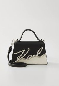 Zwart-witte handtas met een gestructureerde vorm, voorzien van een opvallend zilverkleurig logo-accent en een afneembare schouderriem. Glad lederen textuur.