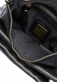 Interno di una borsa a tracolla in pelle nera con più scomparti, dotata di cerniere dorate e una soffice fodera in tessuto scuro. Etichetta di brand notevole all'interno.