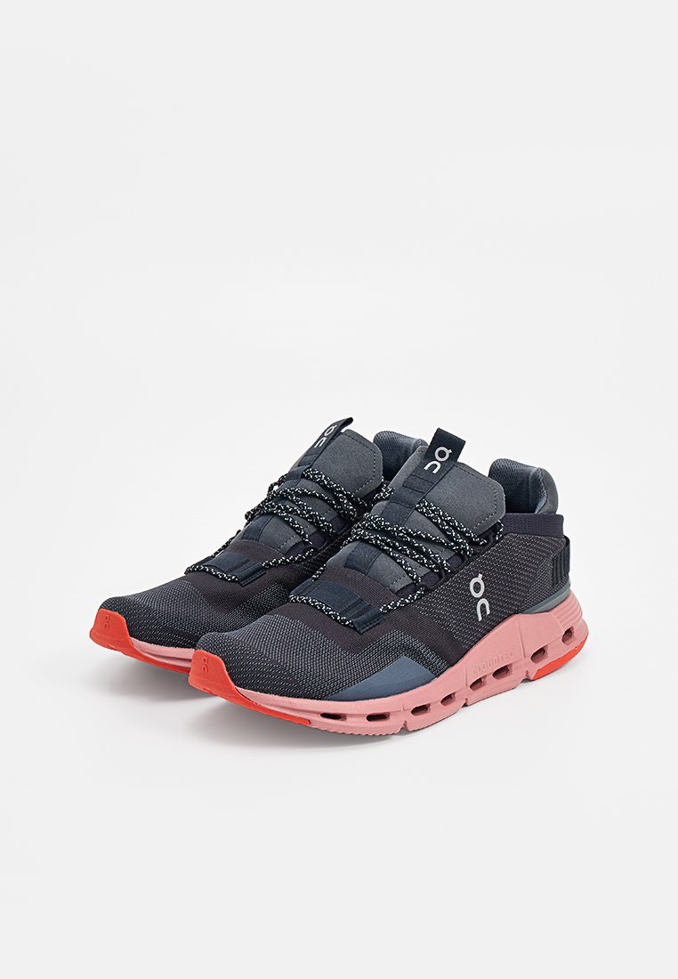 Een paar zwart en donkergrijs sport schoenen met roze zolen en zwart-witte veters, naast elkaar geplaatst op een witte achtergrond.