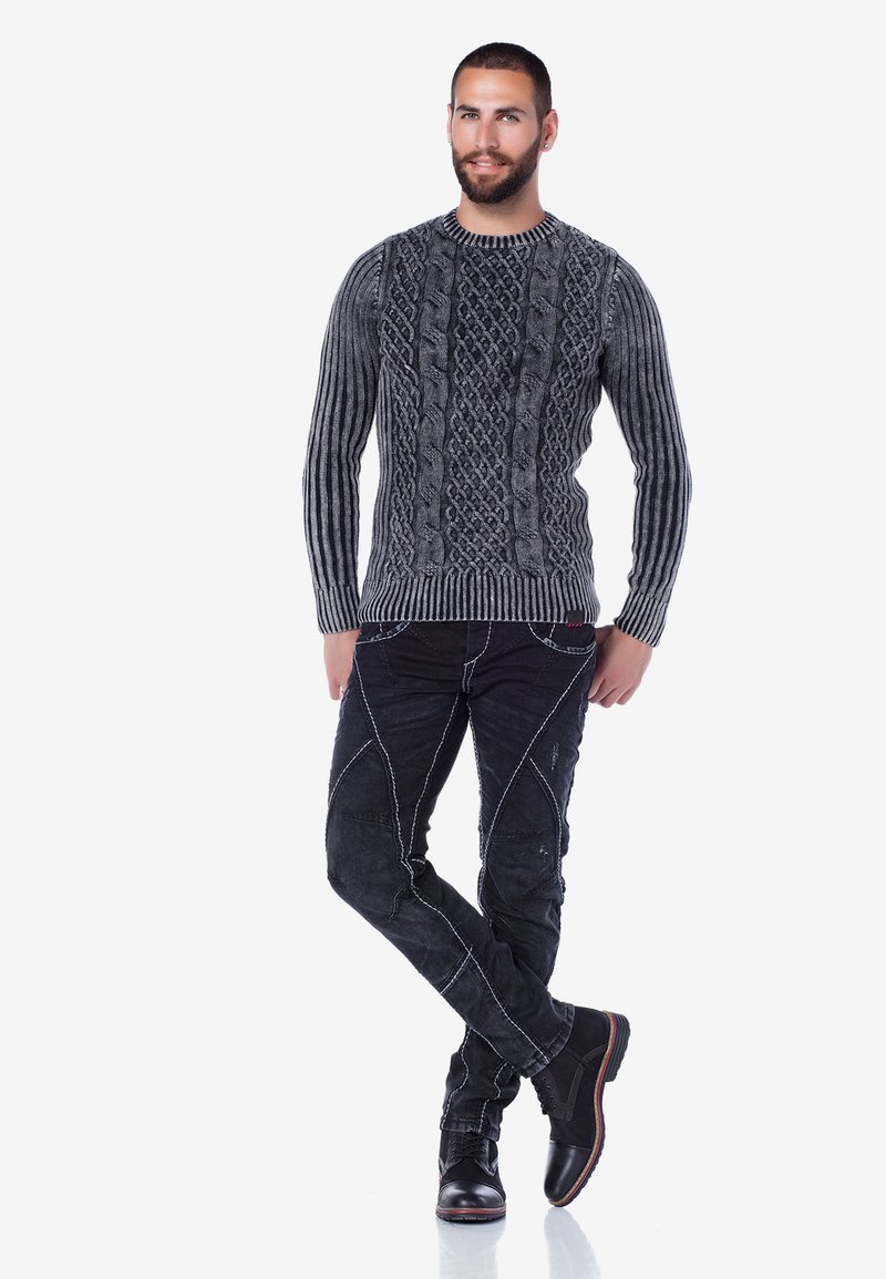Grauer Kabelstrickpullover mit gerippten Ärmeln, schwarze verwaschene Jeans mit weißem Nähten und schwarze Lederstiefel.