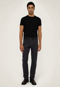 Czarny t-shirt z krótkim rękawem w parze z ciemnoszarymi spodniami o dopasowanym kroju i czarnymi eleganckimi butami. Prosty design z gładką teksturą tkaniny.