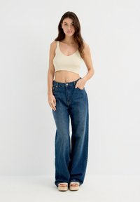 Top corto de canalé crema con tirantes anchos, combinado con jeans de mezclilla azul oscuro de cintura alta y corte holgado. Las sandalias de plataforma completan el look.
