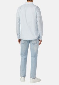 Lichtblauw overhemd met een subtiel patroon, met knopen bij de mouwen en een rugpand, gecombineerd met lichte spijkerbroek en witte sneakers.