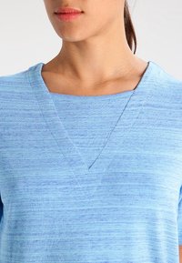 Light blue V-neck top with a textured, lightweight fabric. Features a relaxed fit and subtle horizontal stripes in varying shades of blue.