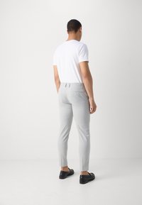 Szare dopasowane spodnie o wąskim kroju, z teksturowanym wzorem, dwoma tylnymi kieszeniami i czarnymi butami na slip-on. Model nosi białą koszulkę.