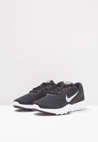 Sneakers nere in mesh con suola bianca, caratterizzate da un prominente logo Nike bianco, punta tonda e superficie testurizzata per la traspirabilità.