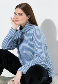 Randig blå polokrage-topp i mjukt tyg, med hög krage och långa ärmar. Kombinerad med svarta manchesterbyxor.