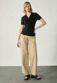 Μαύρη κοντομάνικη μπλούζα με συγκεντρωμένες λεπτομέρειες και κούμπωμα, σε συνδυασμό με μπεζ παντελόνι με φαρδιά πόδια και μαύρες πλατφόρμες.