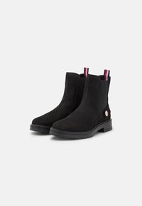 Las botas de tobillo de ante negro tienen una punta redondeada, paneles laterales elásticos y tiradores en rayas rojas, blancas y azules con un acento metálico redondo.