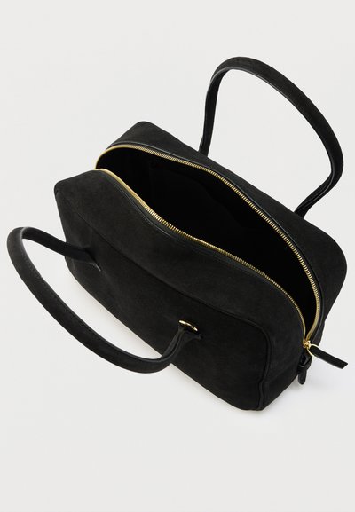 Μαύρη ορθογώνια τσάντα χειρός με χρυστό φερμουάρ, δύο λουριά και ανοιχτό πάνω μέρος που δείχνει το άδειο εσωτερικό, πάνω σε απλό ανοικτόχρωμο φόντο.