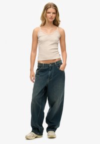 Camisola beige con pizzo, abbinata a jeans in denim scuro a vestibilità ampia. Styling con vita rilassata e due tasche frontali.