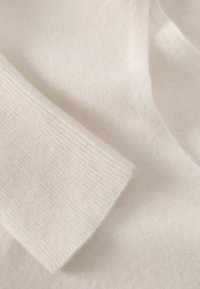 Lyscremefarvet cashmere-sweaterstof med en glat tekstur og ribbet manschet-detalje, vist i et nærbillede.