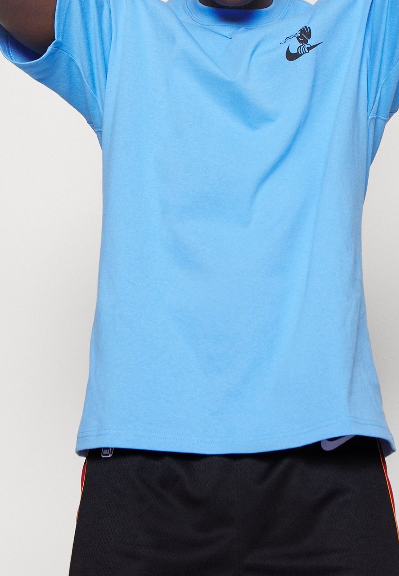 Personne portant un t-shirt bleu clair avec un petit motif noir sur la poitrine et un short de sport noir avec un logo NBA.