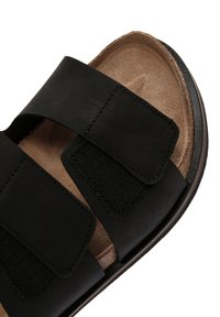 Sandal in pelle nera con due cinturini in velcro regolabili, una soletta testurizzata e una suola marrone con sottili dettagli di cucitura.