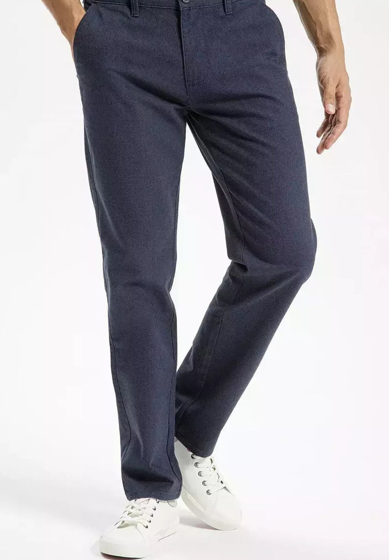 Granatowe spodnie o gładkiej fakturze, klasycznym kroju, subtelnym wzorze i z szlufkami na pasek, połączone z białymi sneakersami.