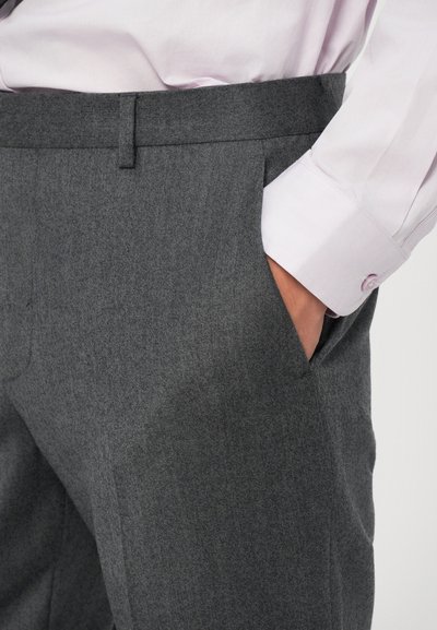Pantalones grises a medida con frente plano, bolsillos laterales y una textura suave. Combinados con una camisa de manga larga color rosa claro.