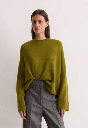 Oversized, long-sleeve, olive green knit sweater with a round neckline, paired with gray, textured, high-waisted trousers featuring side pockets.