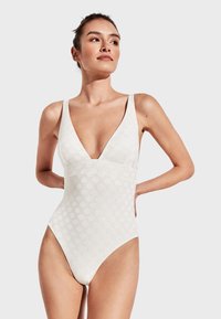 Traje de baño de una sola pieza blanco con un escote en V profundo, textura de puntos, tirantes anchos y piernas con corte alto, confeccionado con una tela suave y elástica.