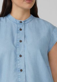 Hellblaues Jeanshemd mit rundem Ausschnitt, kurzen Ärmeln und fünf braunen Knöpfen an der Vorderseite, mit einer glatten Textur.