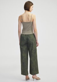 Olivenfarbene weit geschnittene Hosen mit floralem Stickereien und einem hellbraunen Spaghettiträgershirt. Glatter Stoff, lockerer Schnitt, lässiges Design.