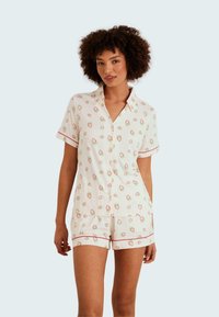 Kortärmad pyjamaset i vit tyg med jordgubbstryck, accentuerad med röd kant, designad för komfort och andningsförmåga.