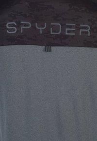 Harmaa urheilupaita, jossa on musta yläosa, jossa on hieno pikselikuvio ja sana "SPYDER" harmaasta, teksturoidusta kankaasta.