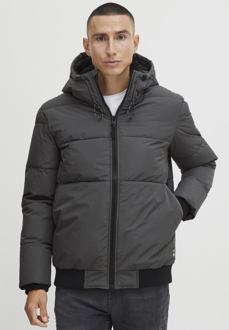 Gray puffer jacket with a zip closure, hood, elastic cuffs, and a ribbed hem. Features stitched panels and side pockets.