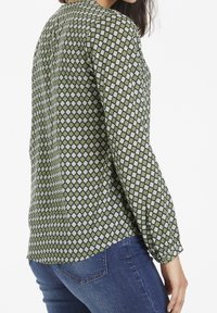 Grøn mønstret bluse med et diamantdesign i creme, lange ærmer, knapmanchetter og en let buet kant. Stoffet virker let.