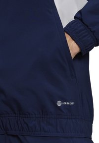 Marineblauwe windbreakerjack met een gestructureerde witte accent, elastische manchetten, zijzakken en een geperst "AEROREADY" logo.