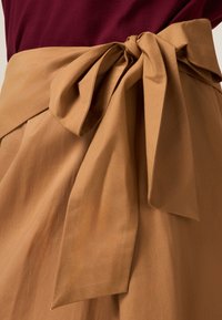 Beiger Wickelgürtel mit großem Schleifendetail. Aus glattem Stoff gefertigt, verfügt er über einen gebundenen Knoten vorne und ein flaches, fließendes Design.