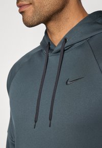 Tumši zils kapuces krekls ar gludu audumu, kuram ir melni aukliņas un diskrets melns Nike logo uz krūšu.