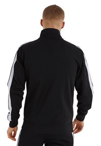 Svart atletisk jacka med hög krage, långa ärmar och vita sidosträck. Tillverkad av ett mjukt, stretchigt tyg.