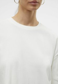 Bílý svetr s kulatým výstřihem, který se vyznačuje jemnou a hladkou texturou a volným střihem. Minimalistický design bez viditelných vzorů nebo akcentů.