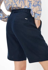 Shorts en lin bleu marine avec une taille élastique, des poches latérales et un petit détail métallique sur la poche arrière. Texture lisse.