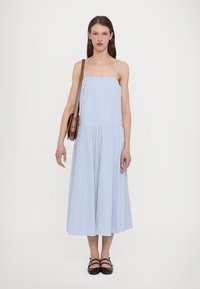 Svetlo modra in bela črtasta midi obleka s tankimi naramnicami, prilegajočim zgornjim delom in razširjenim krilom. Model nosi rjav crossbody torbico.
