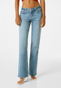 Jeans acampanados de color azul claro, confeccionados en denim, que presentan un diseño de cinco bolsillos y un cierre de cremallera con un solo botón.