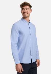 Camicia azzurro chiaro con maniche lunghe, colletto e orlo dritto. Il tessuto appare liscio con una sottile texture.